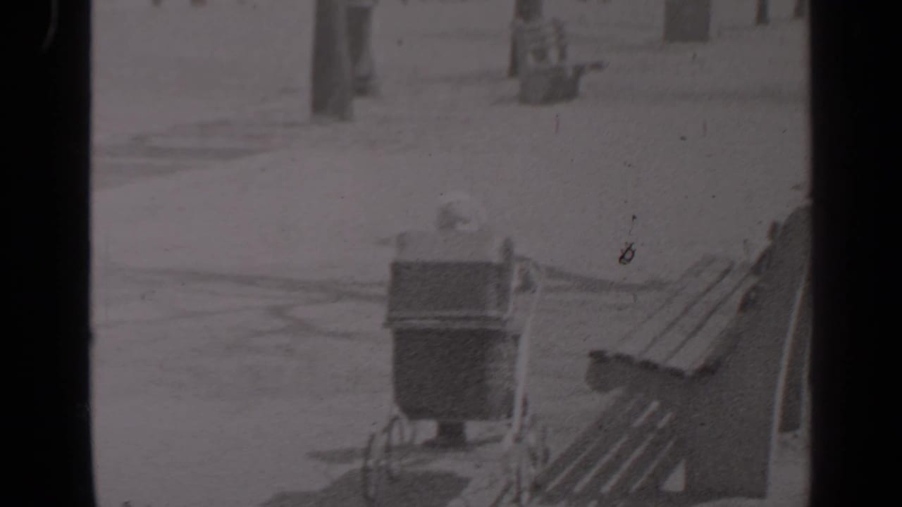 Baby carriage beside wooden park benches on a snowy path.