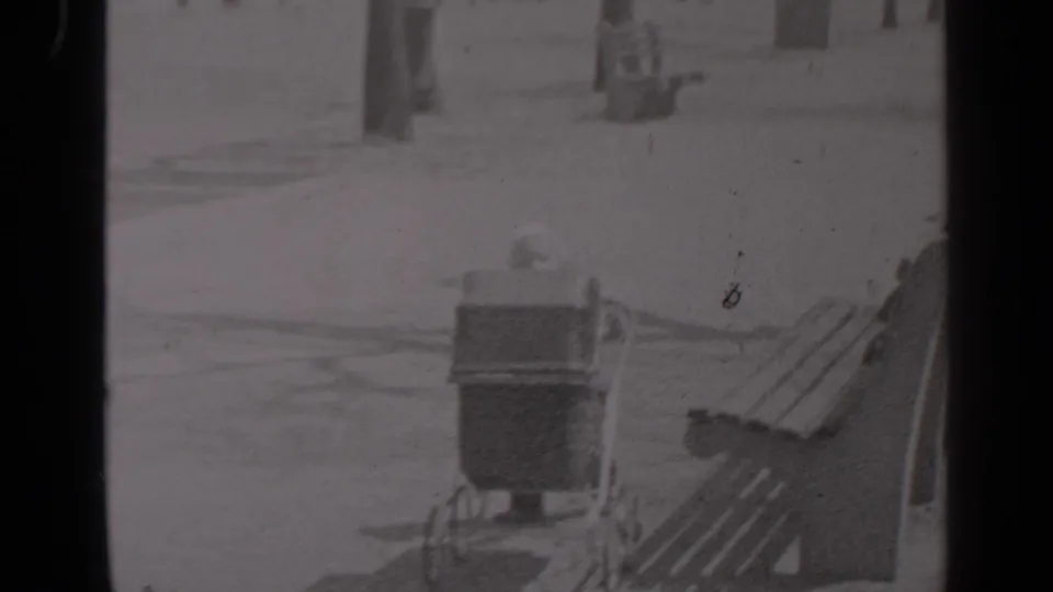 1947 New York home-movie frame showing a vintage baby carriage near wooden benches on a snow-dusted park path.
