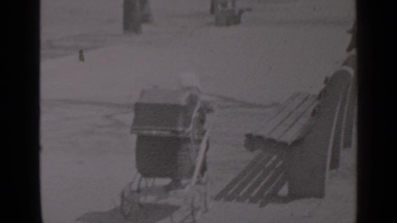 Baby carriage near benches with a small figure partly visible beside it.