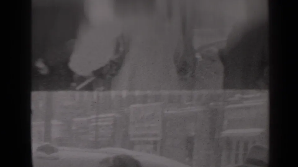 1947 New York home-movie frame showing a soft curbside view with a car edge, railings, and indistinct people in the background.