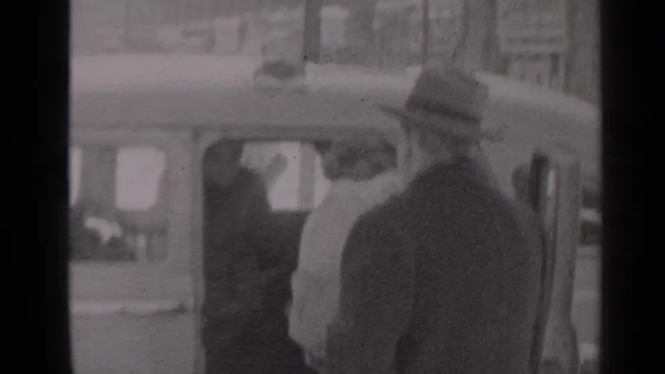 1947 New York frame showing a man in a fedora and dark suit beside a woman at the open car door.