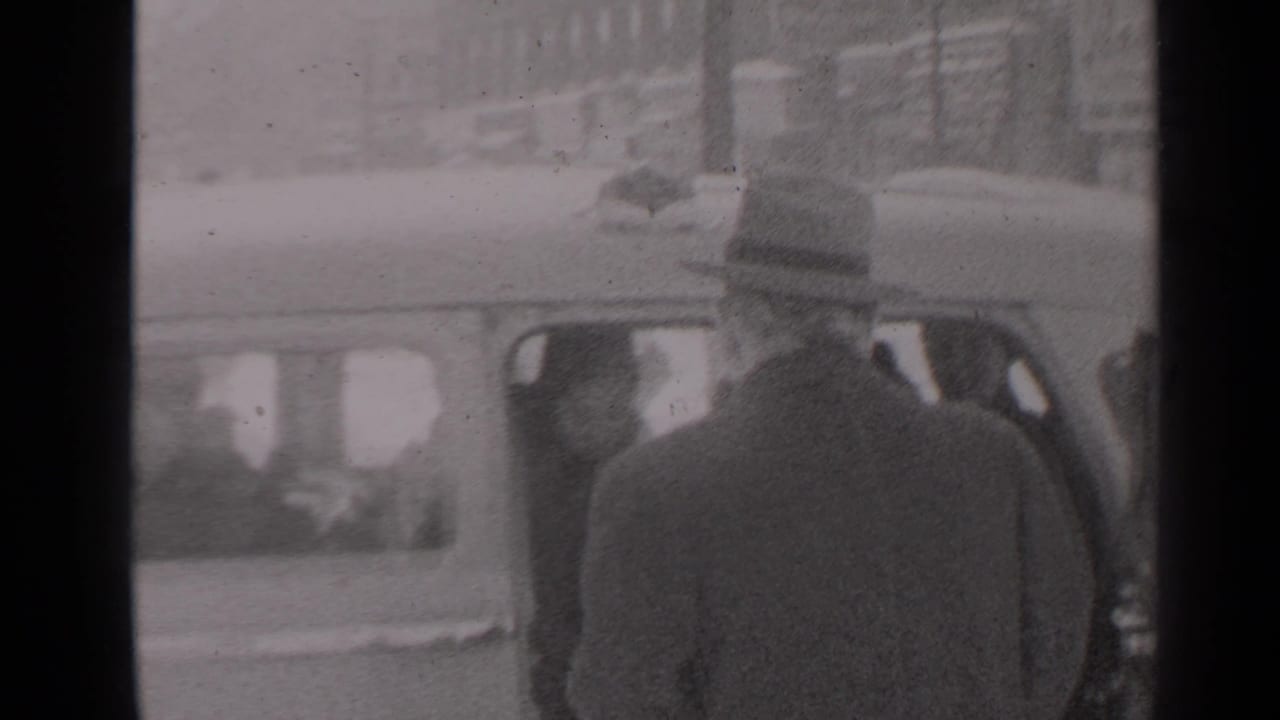 Bundled adults stand near a car outside a snowy house.