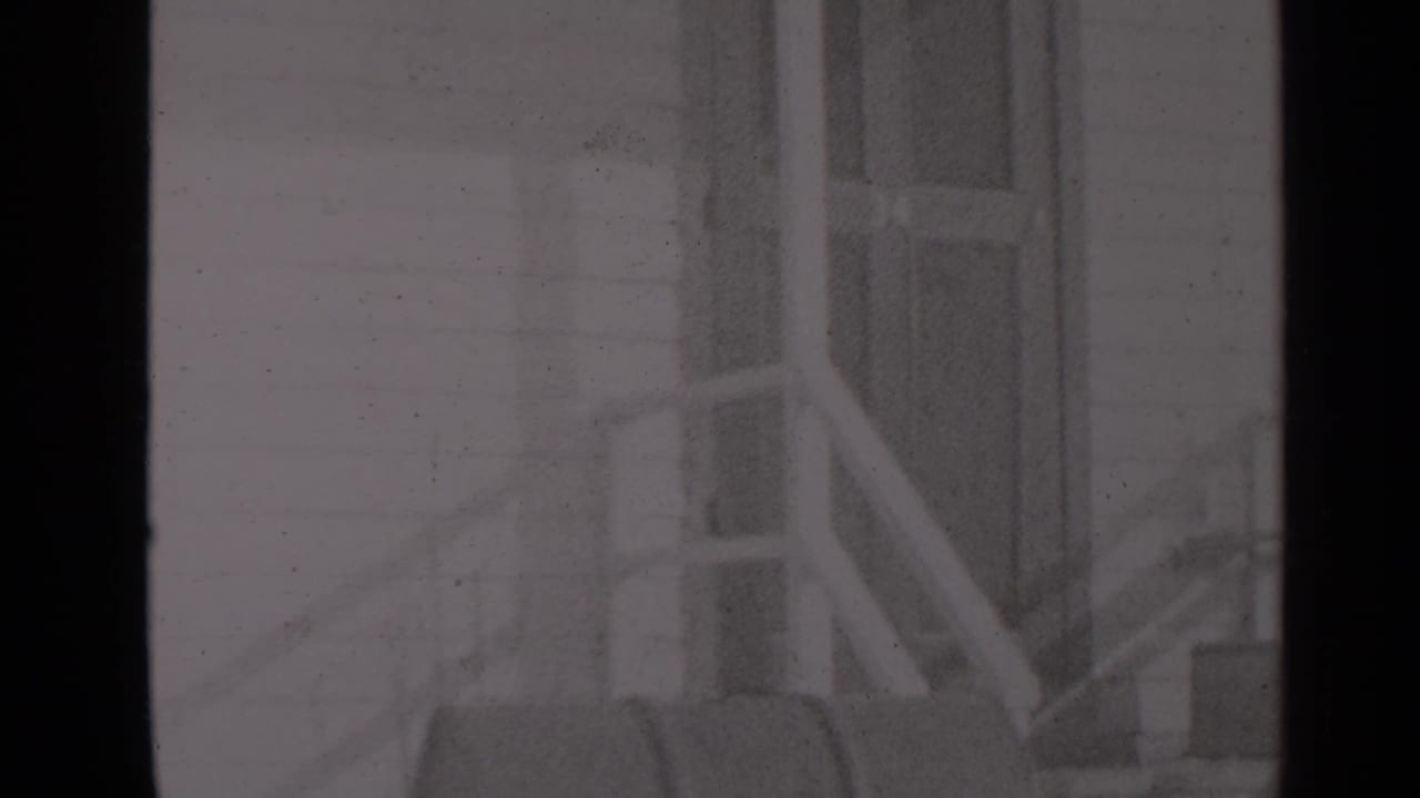 A soft black-and-white frame shows exterior porch steps, railing, and a residential door in the supplied New York winter setting.