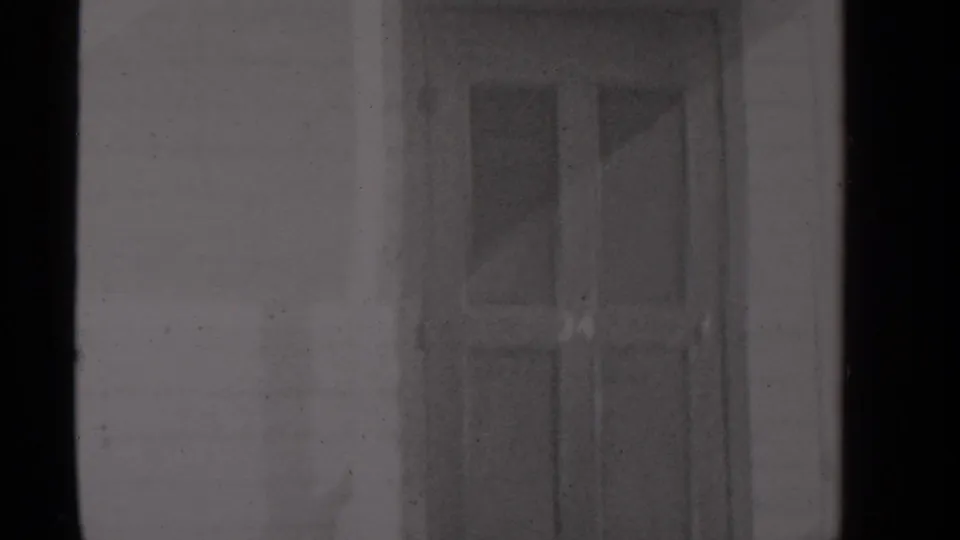 The frame centers on a house entrance, with a door, trim, and snow-softened threshold visible in grainy 8mm footage.