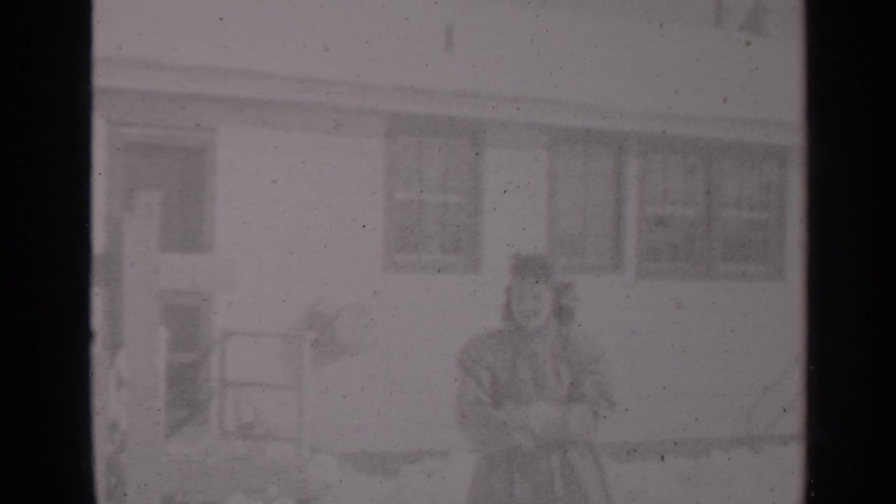 Soft 8mm frame from a 1947 New York winter home movie, with a woman and small child outside a residential building.