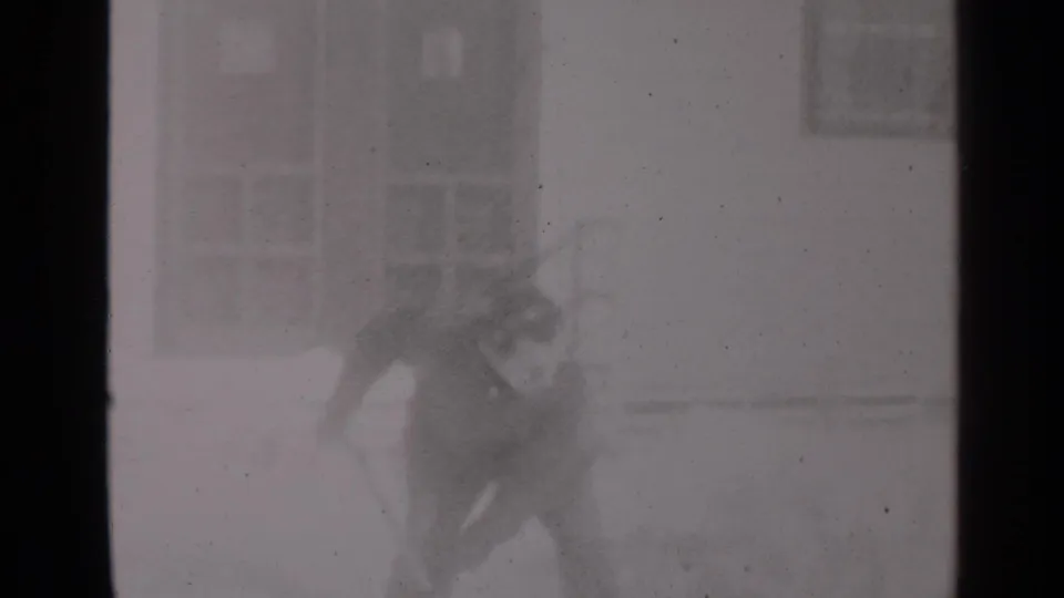 1947 New York home-movie frame showing a man shoveling snow beside a residential building.