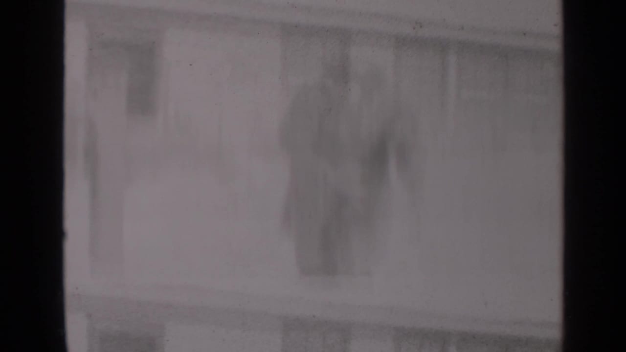 Soft-focus residential windows and snow partly obscured by dark film frame edges.