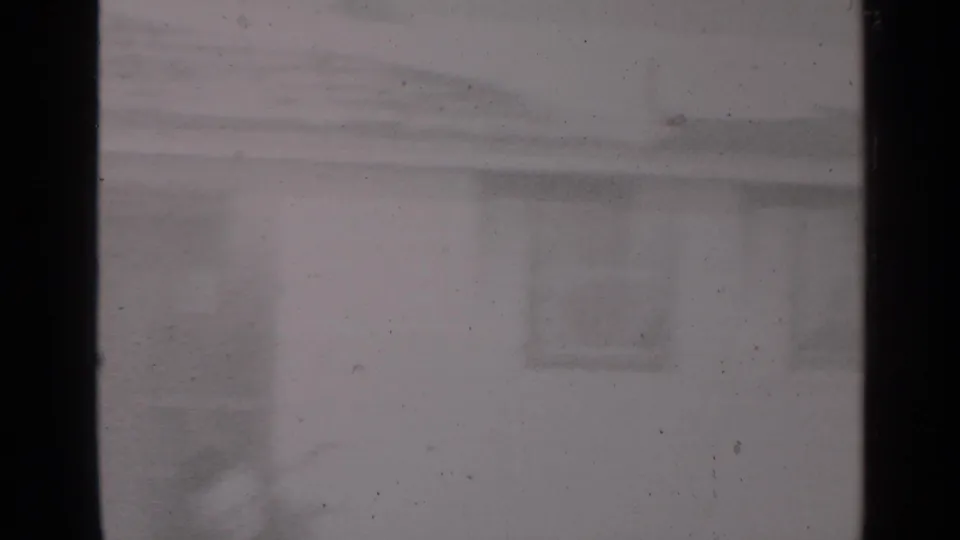 Soft 1947 New York 8mm frame showing a snow-covered residential exterior viewed through a dark interior window frame.