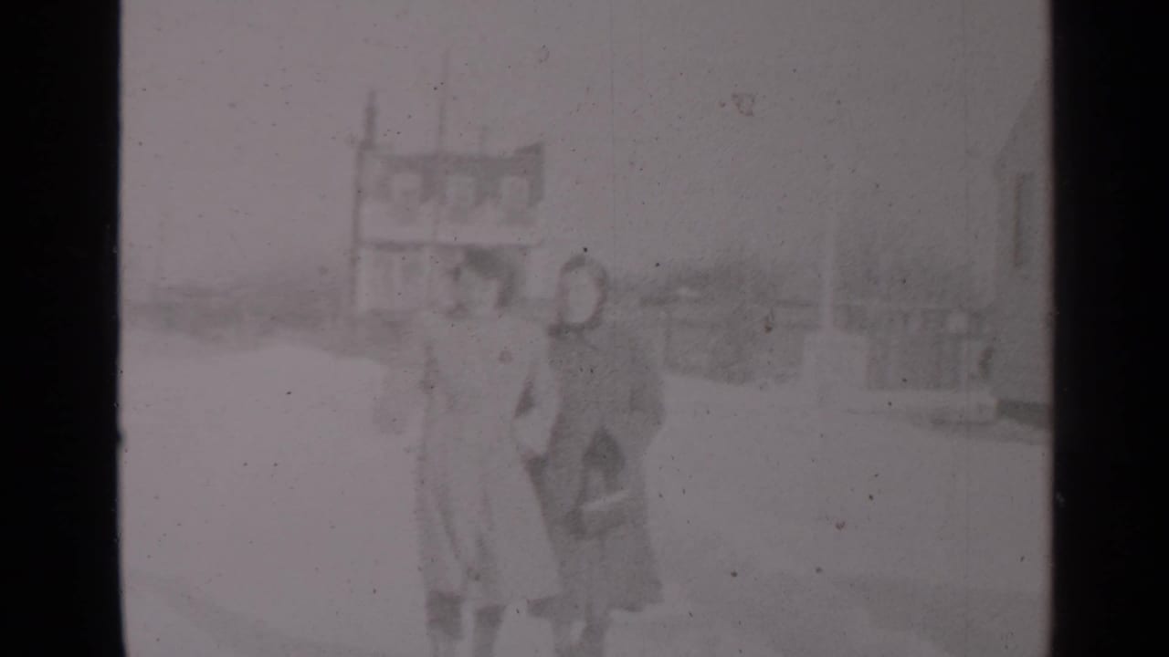 Two bundled women walk arm in arm on a snowy street.
