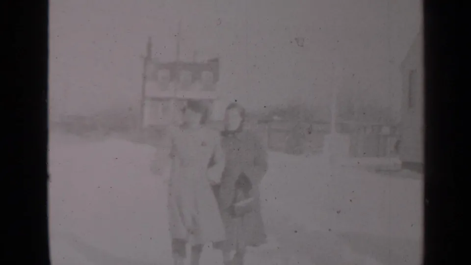 Two women in heavy winter coats walk side by side through snow in 1947 New York home-movie footage.