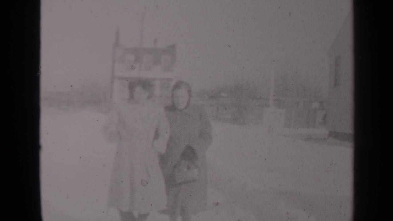 Two women in winter clothing stand or walk close together in snow.