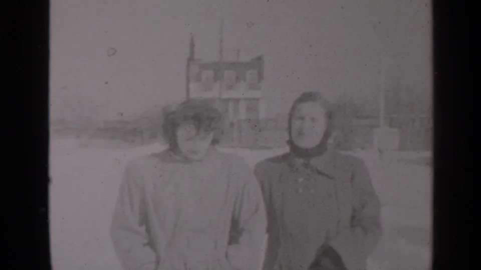 Two women in winter outerwear look toward the camera while walking forward on a snowy New York street in 1947 footage.