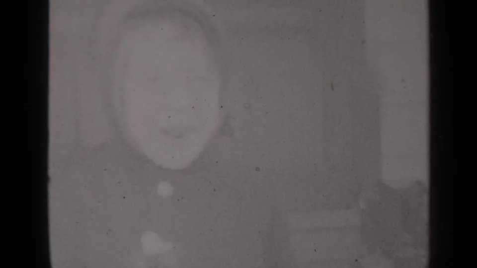Abstract, underexposed 8mm frame with a grey surface, faint circular shape, dust, and soft focus before the doorway scene.