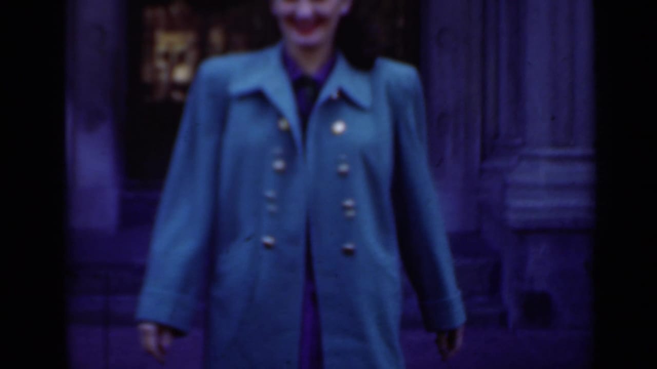 Adult woman in a bright green coat stands near an ornate doorway.
