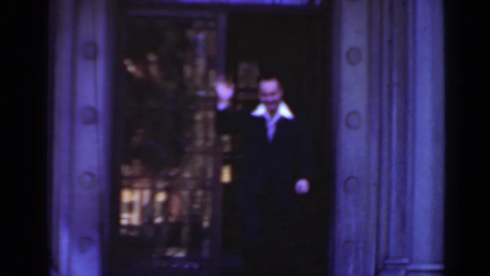 Adult man in a dark suit with a light collar appears at an ornate building entrance in the 1947 New York home-movie footage.