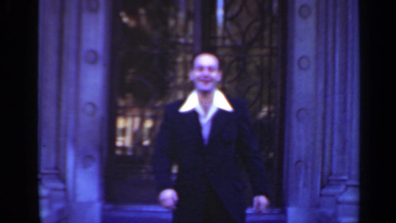 Well-dressed man walking toward the camera outside ornate doors.