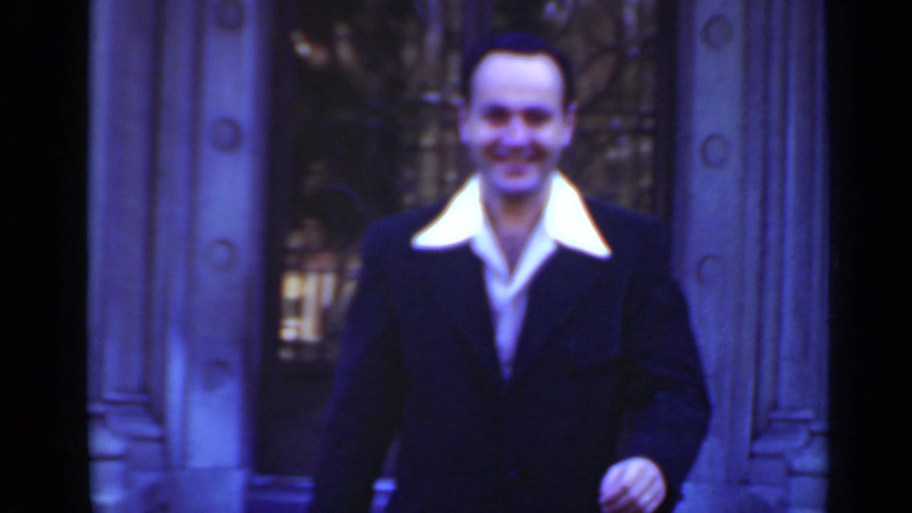 Smiling man in a dark suit near a grand building entrance.