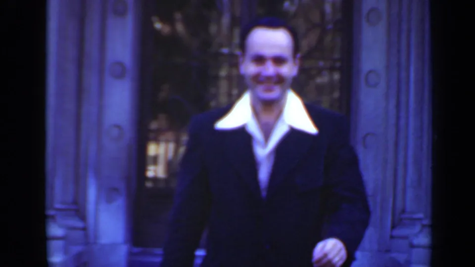 A smiling man in a dark suit stands closer to the camera at a grand entrance in 1947 New York home-movie footage.