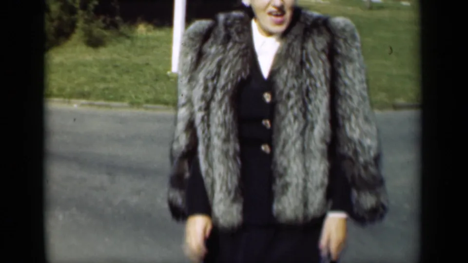 The final frame gives a close view of the woman’s fur coat and dark dress, with the paved street and grass lawn still visible behind her.