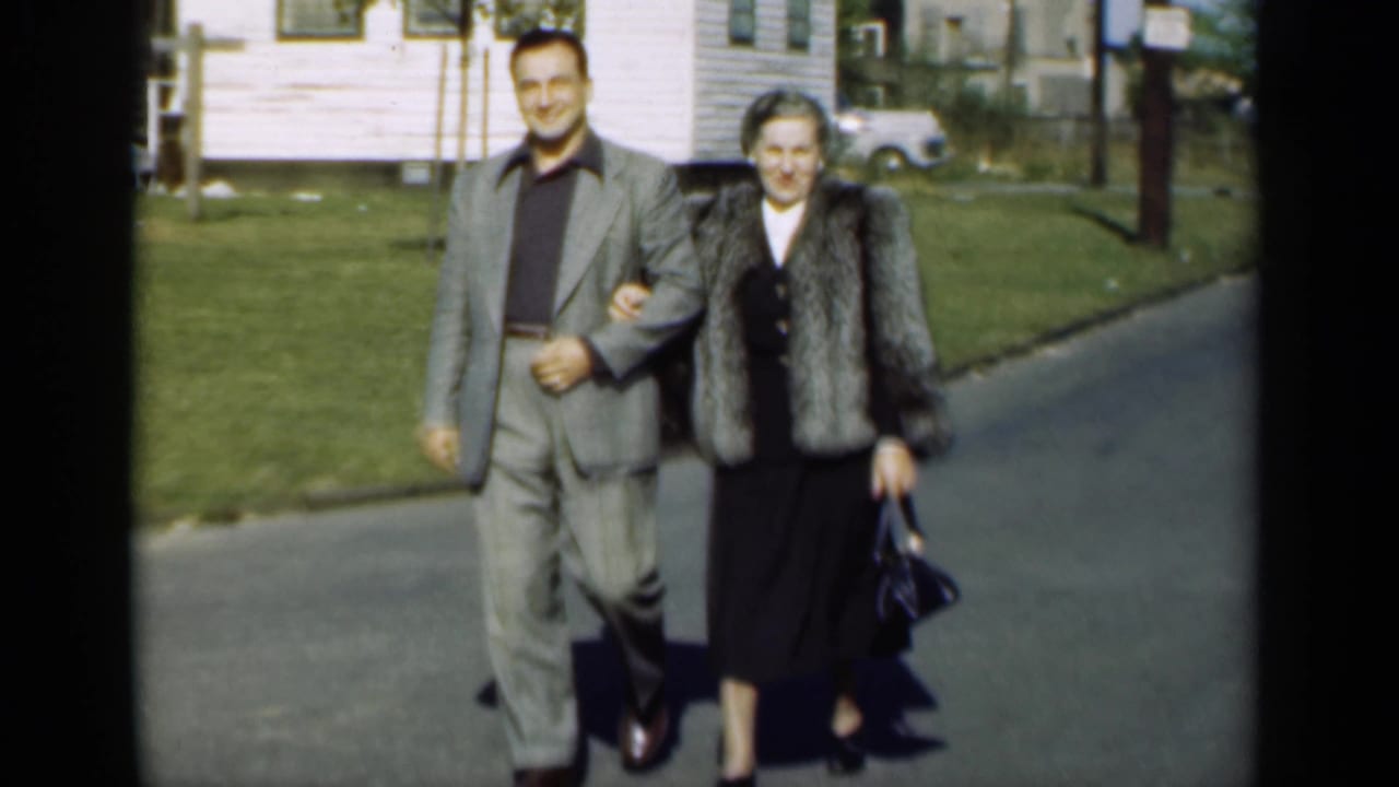 A smiling couple walks together on a street, with the woman carrying a dark handbag.