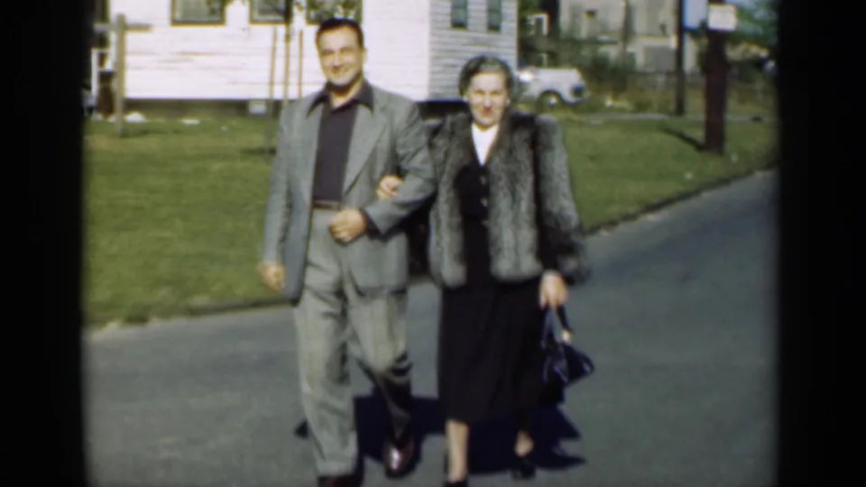 The couple continues along a New York residential street, smiling as they walk arm-in-arm in mid-century dress.