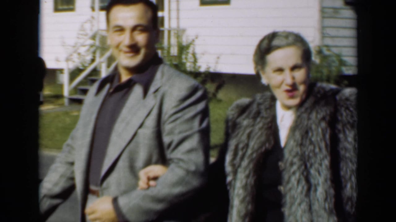 The couple continues walking outdoors, with the man facing the camera and the woman beside him.