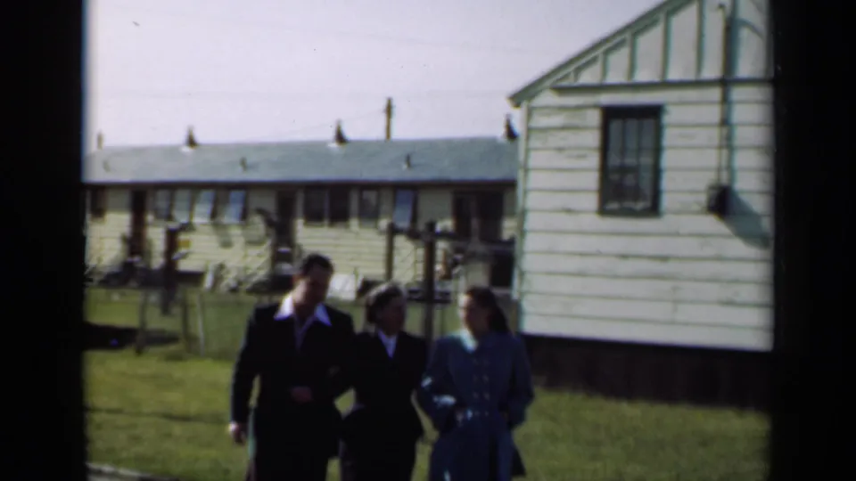 A later frame shows three adults walking near similar residential buildings and lawns, likely part of the same home-movie sequence.