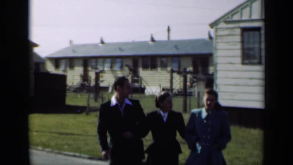 A man and two women in tailored clothing walk forward on a lawn in a New York home-movie scene from 1947.