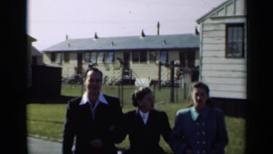 The group reaches the foreground, with their 1940s clothing visible against a lawn and simple New York residential buildings.
