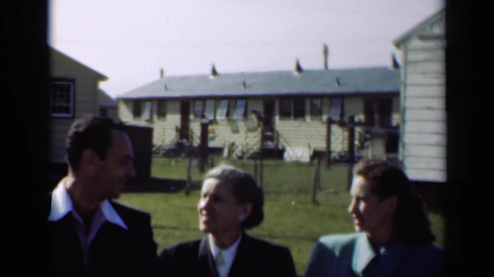 The companions pass nearer to the camera, their faces partly shadowed, with residential buildings and a lawn in the background.