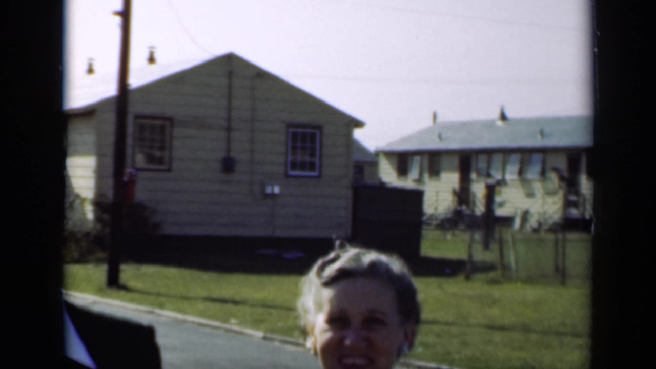 Older woman smiling near the camera with small houses and lawns behind her.