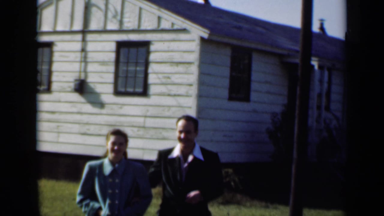 Young couple standing outside a light-sided house in bright daylight.