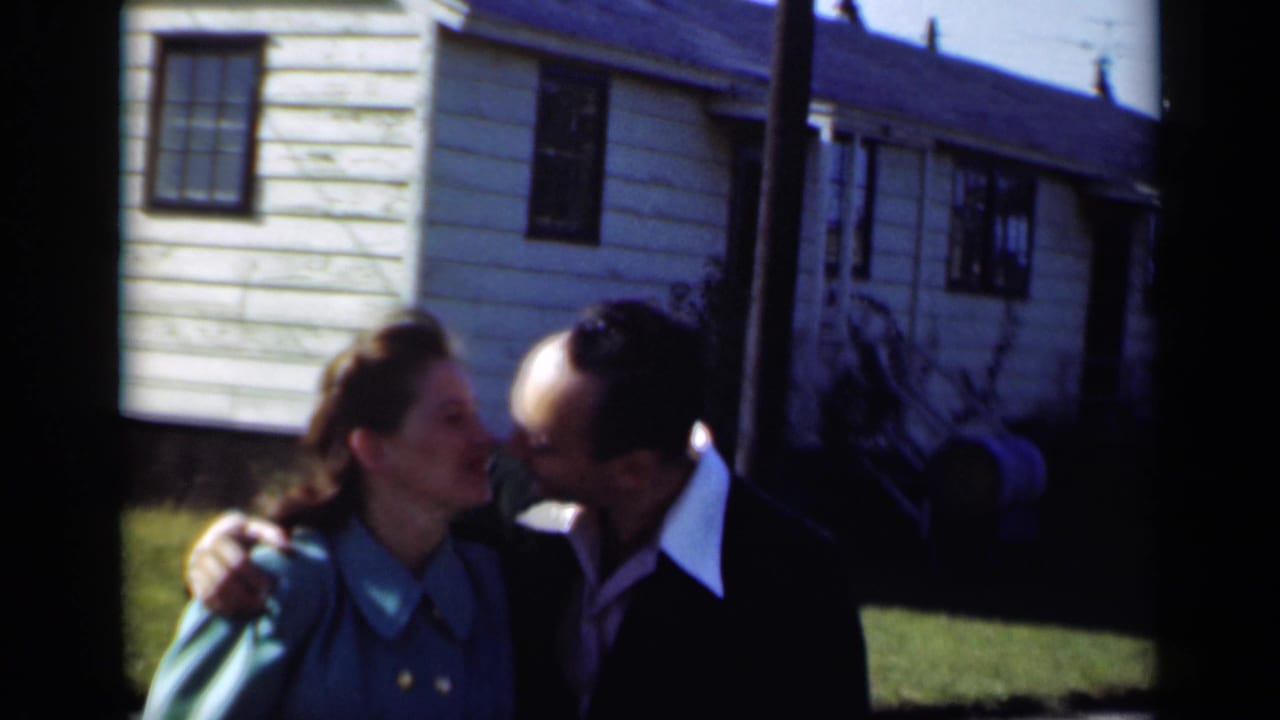 Couple standing close outside a white clapboard house as the man leans toward the woman.
