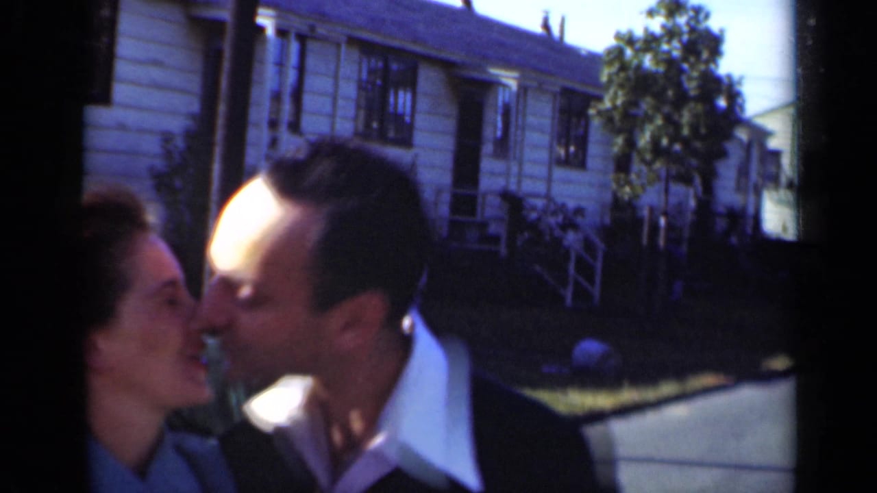Close view of a couple kissing in front of a clapboard residential building.