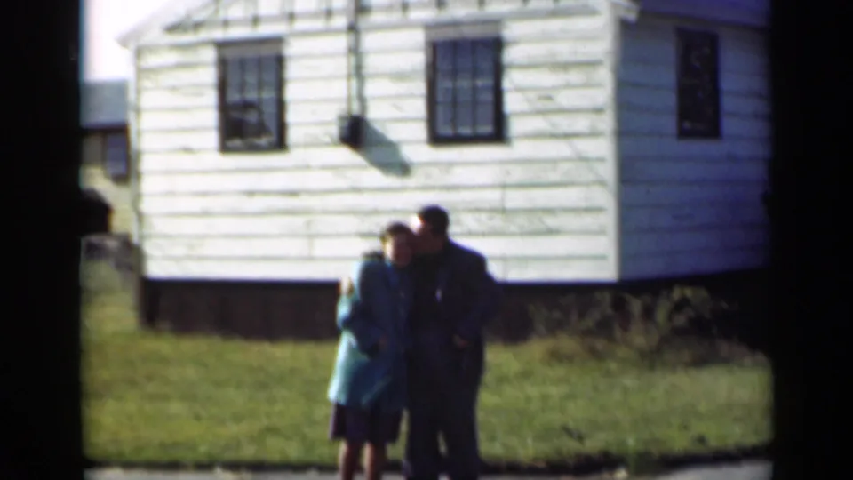 A wider 8mm view shows the couple embracing near a white clapboard house in the supported 1947 New York setting.