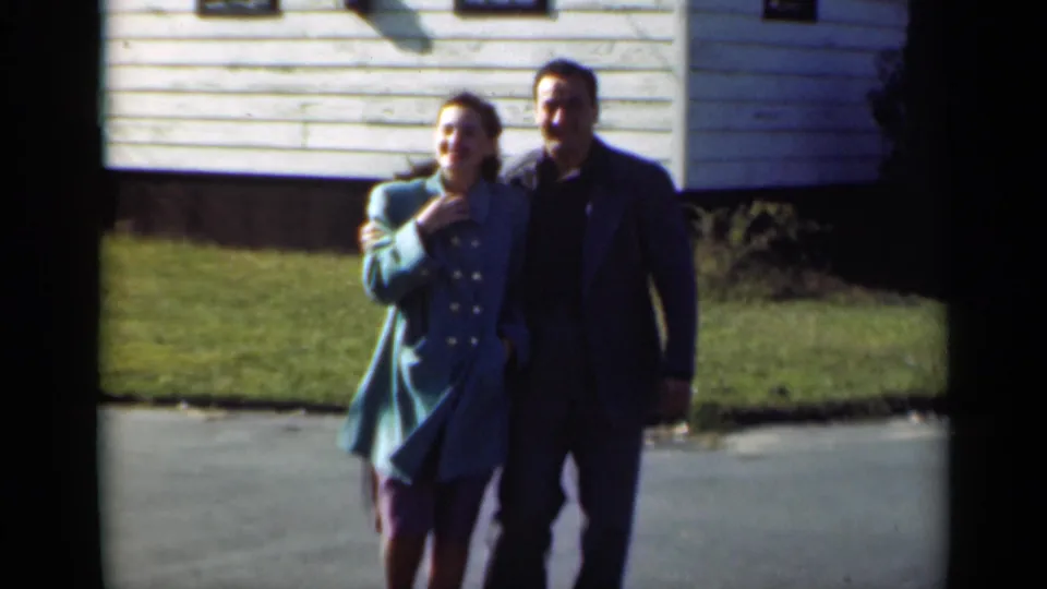 A smiling young couple walks toward the camera in this 1947 New York home-movie view of a residential street.