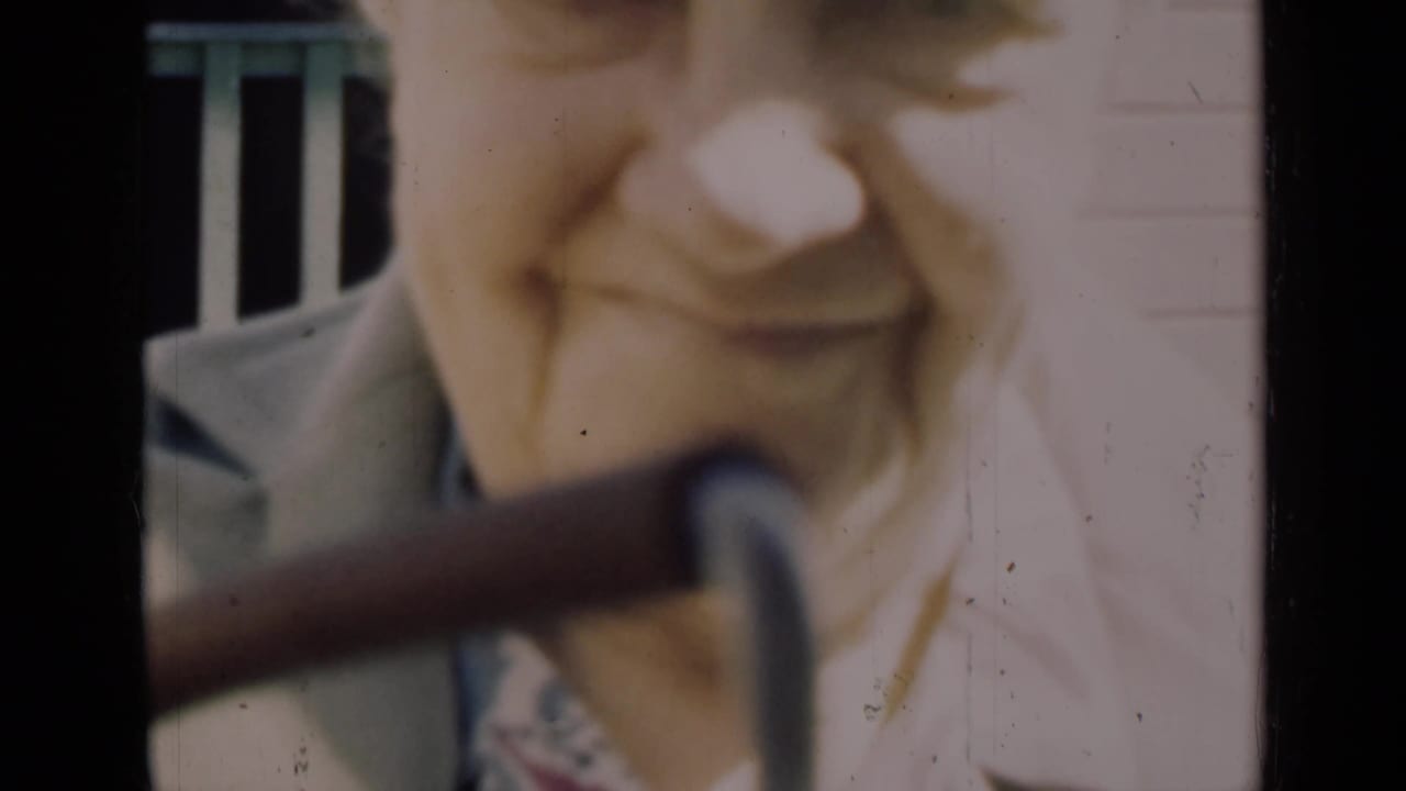 Close 1948 Indiana home-movie view of an elderly woman smiling warmly as a dark pipe or railing crosses the frame.