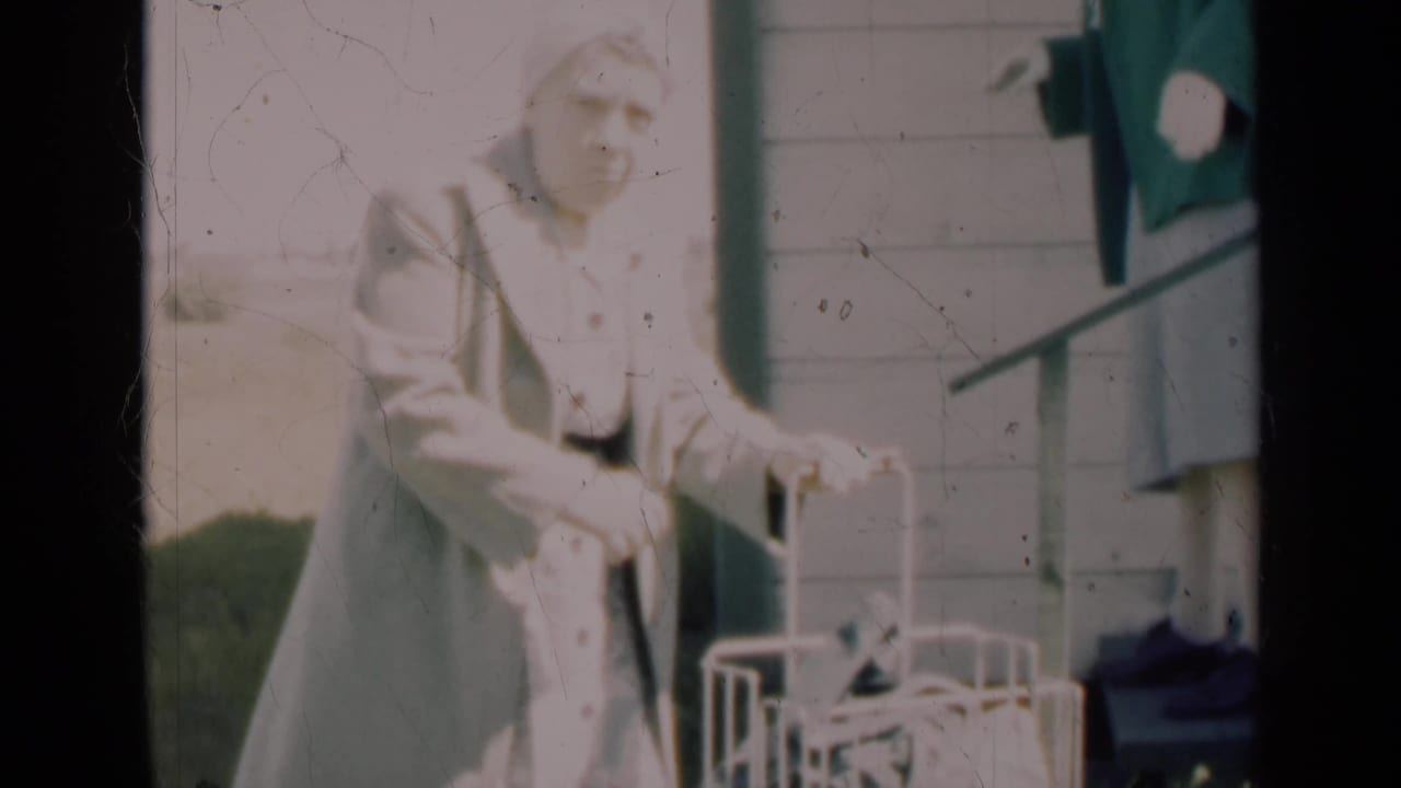 A woman in a light coat and hat handles a white carrier outside, with another woman in a green jacket standing near the steps.