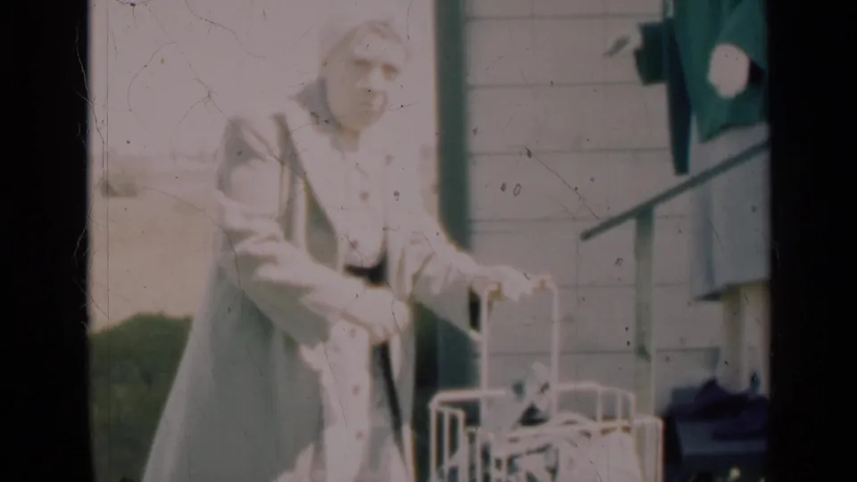 A woman in a light coat and hat handles a white carrier outside, with another woman in a green jacket standing near the steps.