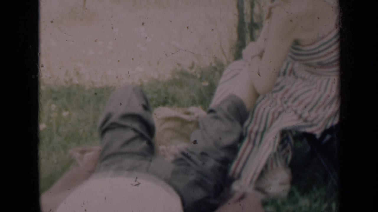 Woman in striped dress leans near a reclining man on grass beside a towel.