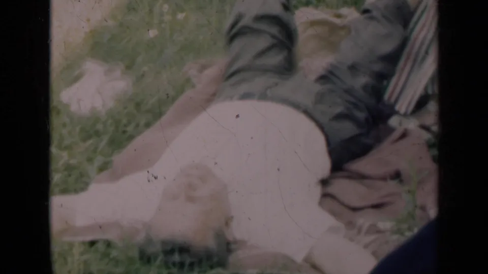 1948 Indiana home-movie frame showing a man lying on grass with a woman seated close by in a striped dress.