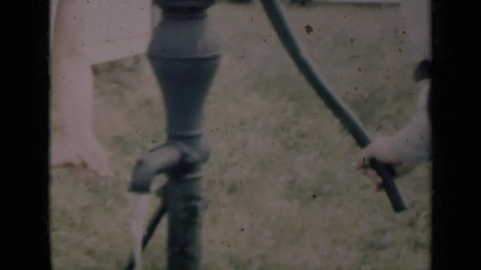 A closer 8mm view shows the hand pump body and handle while an adult operates it in an outdoor grassy area.