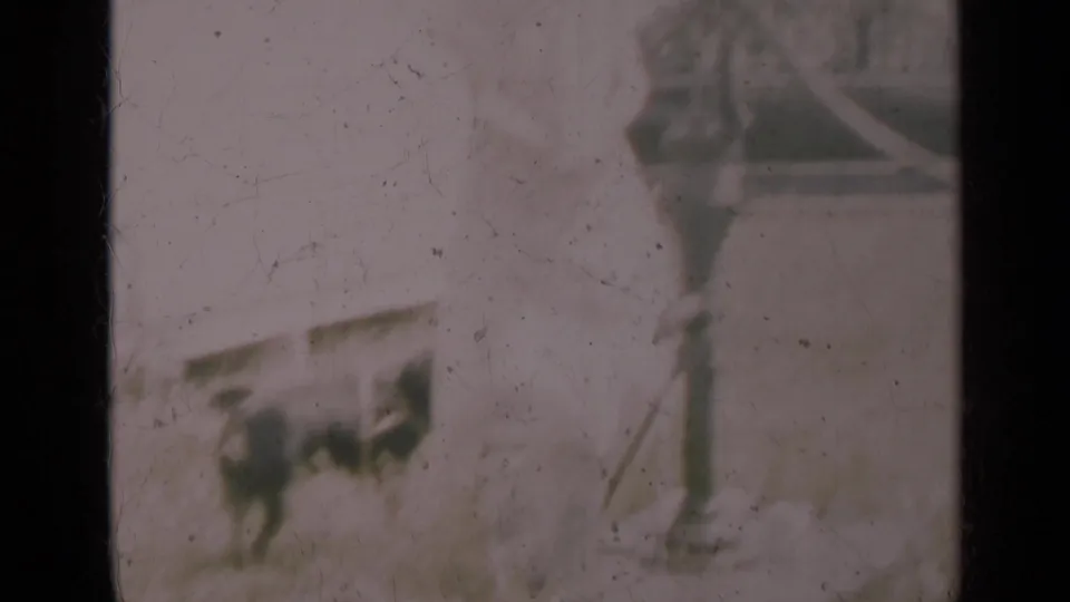 A dog stands beside the hand pump in the Indiana outdoor scene, with an adult partly visible and a vintage car in the background.