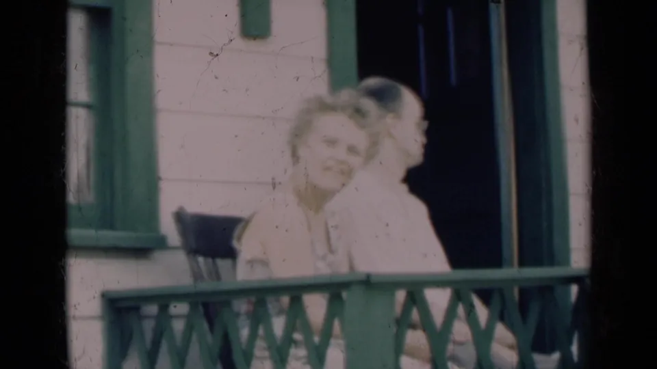 An older couple sits near a porch railing and dark doorway, with the woman turning toward the camera in 1948 Indiana footage.