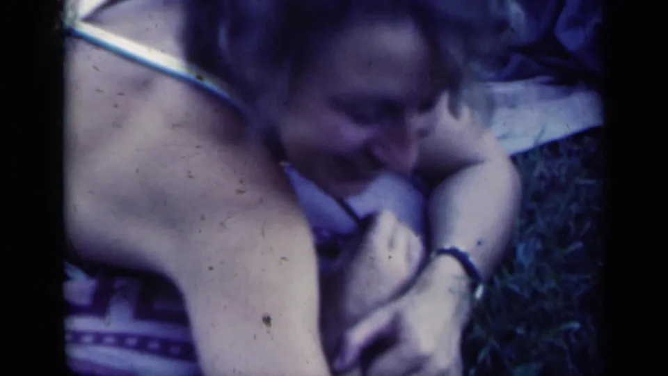Close 8mm frame of a woman reclining on grass in Indiana, her face partly turned down and arm resting near her cheek.