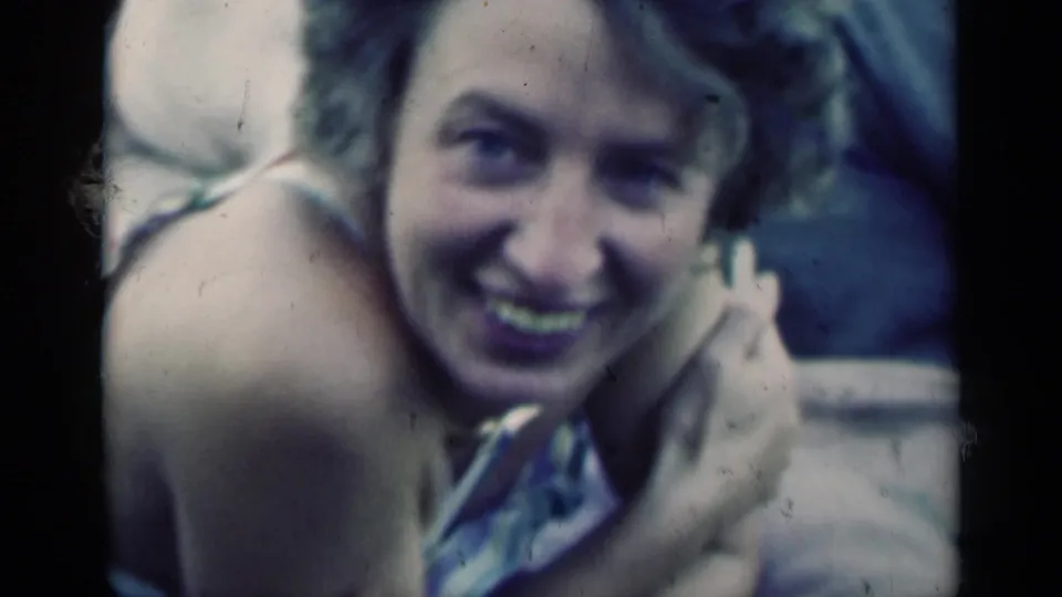In this Indiana home-movie frame, the young woman smiles directly at the camera with her hand resting near her face.