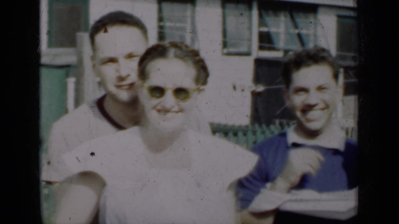 Three young adults pose outdoors near a house and fence.