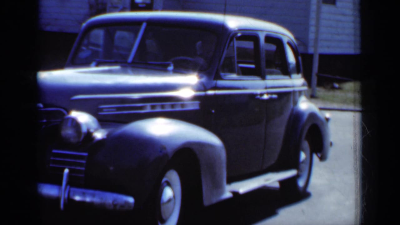 Dark sedan viewed from the front side with strong sunlight across the hood.