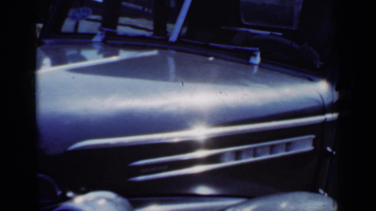 Close view of a vintage car hood and side trim with windshield and dashboard partly visible.