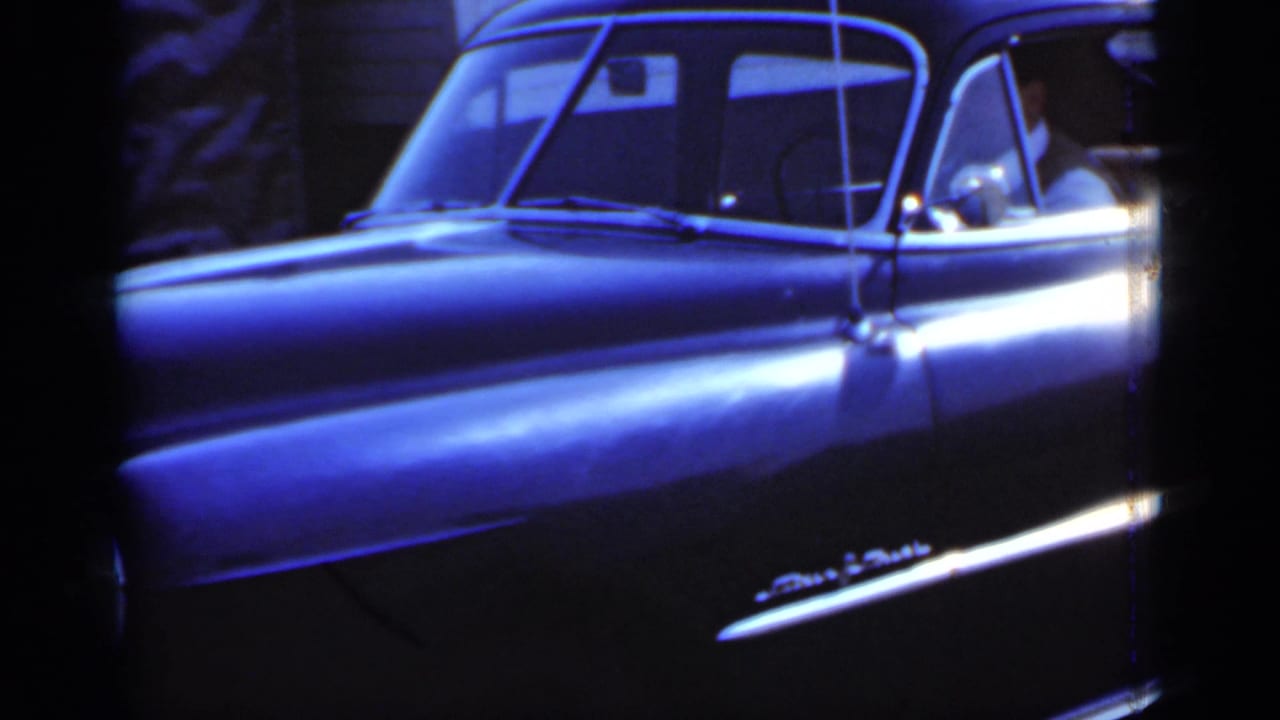 Dark classic sedan in bright sunlight with a driver visible through the front window.